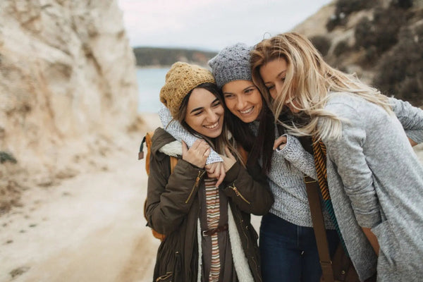 Drei junge Frauen in warmer Kleidung lachen herzlich miteinander, stehen eng umarmt, symbolisieren Verbundenheit und Freundschaft